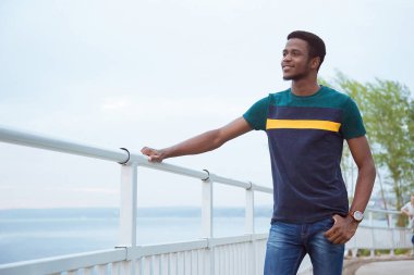 Siyahi bir adam, bir adam çitte el alıştırması yapıyor. Nazik, dostane bir gülümseme. Baraj, sahil. Değişim öğrencisi. Uzayı kopyala Nehir ve denizin arka planına karşı bir değişim öğrencisi..