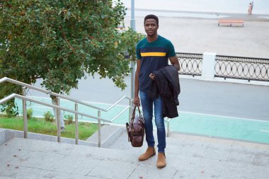 Zenci genç bir adam elinde bir çanta ve paltoyla şehrin merdivenlerinden aşağı iniyor. Göçmenlik, turizm, Avrupa 'da değişim öğrencisi. Modaya uygun giyinen adam. Yaşam tarzı.