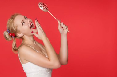 Güzel bir genç anime kızı elinde kırmızı beyaz bir lolipop tutuyor ve gülümsüyor. Saç kesimi, çocukluk ve ciddiyetsizlik olan sarışın bir kadın..