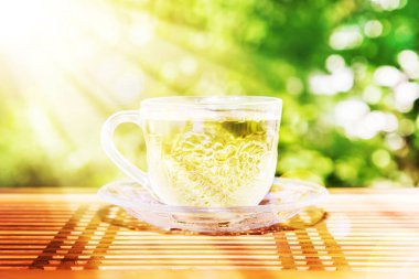 Yeşil arka plandaki masada bir fincan yeşil çay. Güneş Işını. Yaz günü.