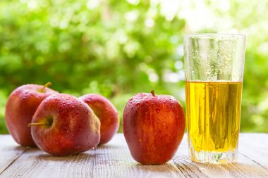 Bahçedeki masada kırmızı elmalarla birlikte bir bardakta elma şarabı. Doğal bir geçmişi olan taze elma suyu, sağlıklı yiyecekler..