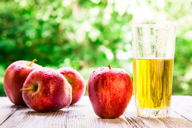 Bahçedeki masada kırmızı elmalarla birlikte bir bardakta elma şarabı. Doğal bir geçmişi olan taze elma suyu, sağlıklı yiyecekler..