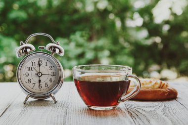 A wooden countertop on a blur of fresh green abstract background. Clock on the table in the green garden at 6 pm, bakery, patty, black tea, tea party clipart