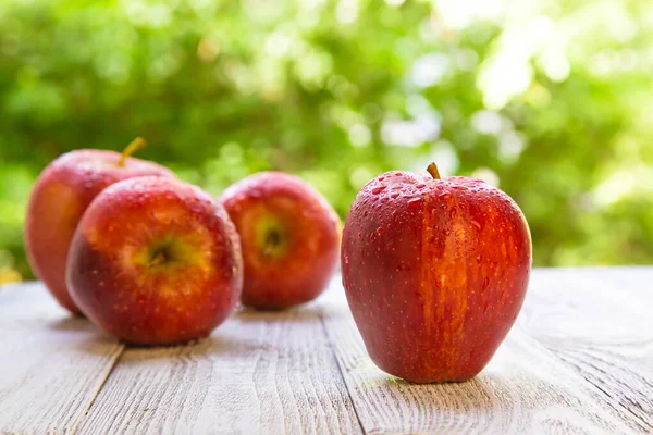 Four red juicy apples on a wooden board, table, against a background of green, blurred foliage. A gray board. Healthy diet, diet.