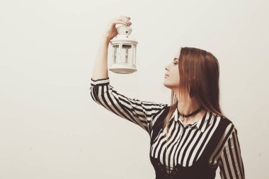 Çizgili gömlekli ve korseli güzel bir kadın elinde beyaz bir fener tutuyor. Boşluğu kopyala, metnin buraya.