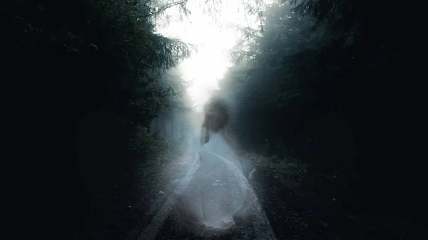 Kışın, ağaçların sisle örtülü olduğu ürkütücü, ürkütücü bir orman. Beyazlı, şeffaf bir kadın yolda yürüyor.. — Stok fotoğraf