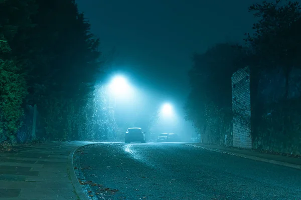 An dark mysterious eerie, English road with street lights on an atmospheric foggy winters night. UK — Stock Photo, Image