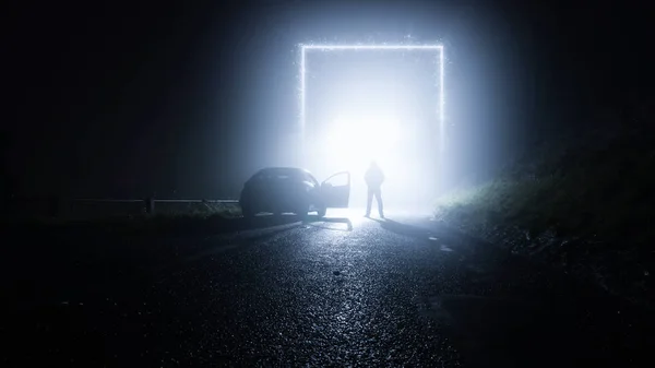Um portal reluzente, porta de entrada numa estrada rural. Com um homem ao lado de um carro. Numa noite assustadora, nebulosa e invernal. Conceito de ficção científica . — Fotografia de Stock