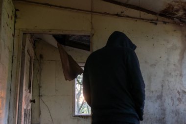 Yıkık ve terk edilmiş bir evde gizemli bir kukuletanın arkasına bakıyorum. karanlık, karamsar düzenleme.