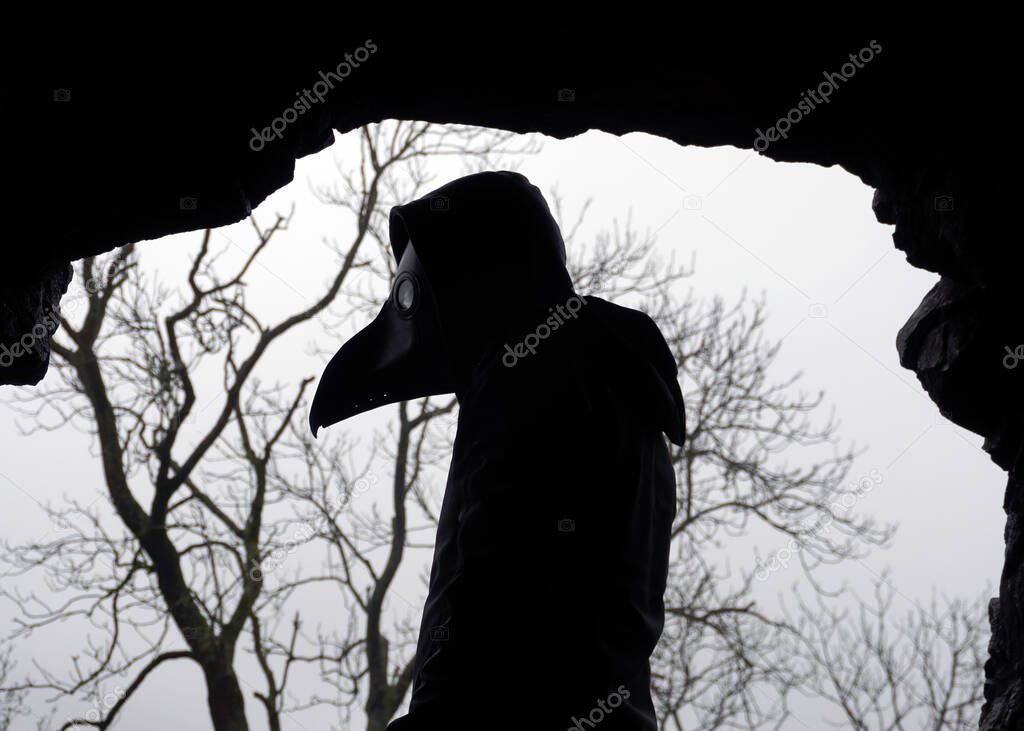 A scary hooded figure wearing a Halloween plague doctors mask. Standing in a cave. 