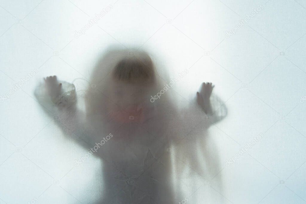 A scary edit of an old doll holding its hands up, shot through a semi transparent material. Creating a textured, blurred, still life.