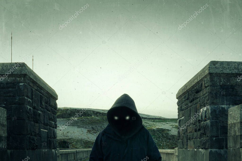 A scary, hooded figure with glowing evil eyes and blank black space where his face should be, standing on a road in the countryside in winter. With a vintage, textured grunge edit.