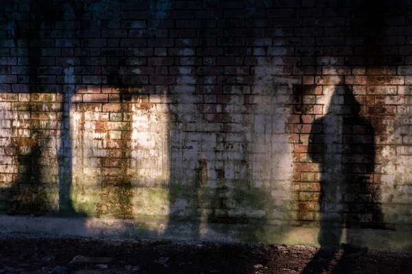 A shadow of a hooded figure standing next to a brick wall. In an abandoned building