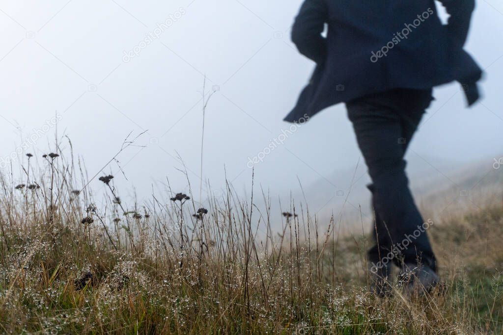 A mysterious figure wearing a coat running in the background, out of focus, in a field on a misty winters day