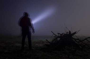 Kapüşonlu bir figürün, sisli bir kış gecesinde meşaleyi parlatması..