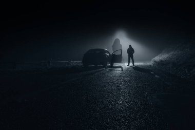 Gece bir köy yolunda yüzen, bulanık elbiseli bir hayalet kadın. Arkasında bir araba ve sürücü var..