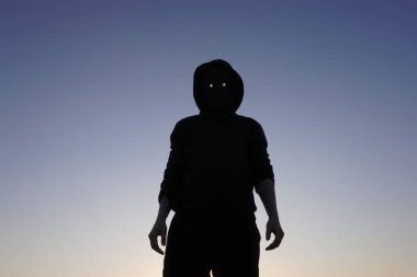 Yüzünün kameraya bakması gereken yerde parlayan şeytani gözleri ve boş siyah alanı olan korkunç, kapüşonlu bir figür.                      