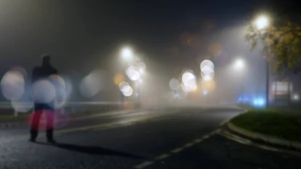霧の夜に道の真ん中に謎の人物が立っている ぼんやりしたボケでフォーカス編集なしで — ストック写真