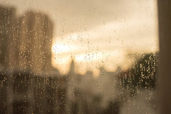 Gotas de lluvia en la ventana de cristal. con edificios borrosos y tono cálido — Foto de Stock