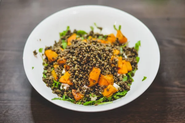 Een plaat met gezonde pompoen en linzen salade op een donkere houten tafel. — Stockfoto