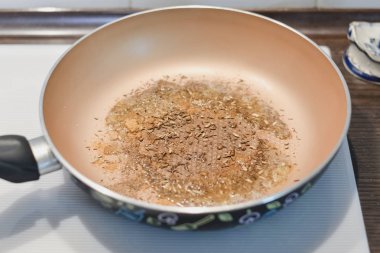 Farklı baharatlar sağlıklı Ayurveda çanak khichdi beyaz bir soba üzerinde hazırlanması için derin bir tavada ısıtılır.