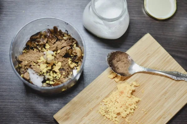 Healthy sugar-free cocoa dough in a food processor and orange zest on a wooden board for truffles on a dark wooden table.