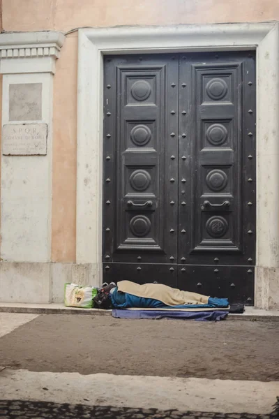 ROME, ITALY - CIRCA OCTOBER 2016: a homeless man sleeps at the big old doors in the historical center of Rome, Italy  at night circa October 2016. — Stock Photo, Image