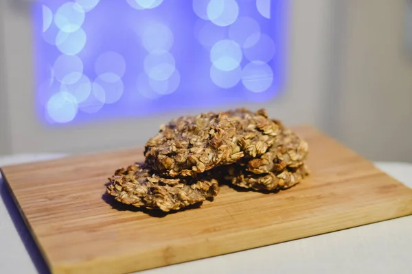 Galletas saludables sin azúcar y sin harina de plátano y avena en una tabla de madera con luces festivas en el fondo . —  Fotos de Stock