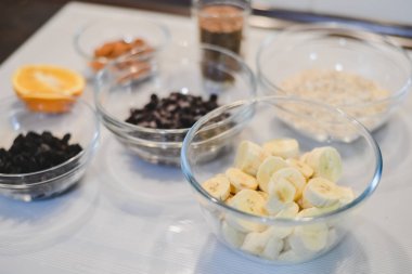 Bir sağlıklı şekersiz için malzemeler ve un ücretsiz muz yulaf ezmesi muffins: kesilmiş muz, böğürtlen, Kuru üzüm, badem, yulaf, bir cam kase ve bir yarım veya bir portakal beyaz bir yüzeye keten tohumu.