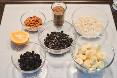 Bir sağlıklı şekersiz için malzemeler ve un ücretsiz muz yulaf ezmesi muffins: kesilmiş muz, böğürtlen, Kuru üzüm, badem, yulaf, bir cam kase ve bir yarım veya bir portakal beyaz bir yüzeye keten tohumu.