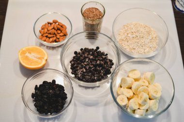 Bir sağlıklı şekersiz için malzemeler ve un ücretsiz muz yulaf ezmesi muffins: kesilmiş muz, böğürtlen, Kuru üzüm, badem, yulaf, bir cam kase ve bir yarım veya bir portakal beyaz bir yüzeye keten tohumu.