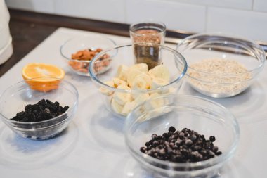 Bir sağlıklı şekersiz için malzemeler ve un ücretsiz muz yulaf ezmesi muffins: kesilmiş muz, böğürtlen, Kuru üzüm, badem, yulaf, bir cam kase ve bir yarım veya bir portakal beyaz bir yüzeye keten tohumu.