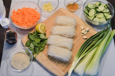 Bir Asya yemek için malzemeler: cam erişte, salatalık, havuç, soya sosu, susam, sarımsak, zencefil, kereviz, maydanoz ve taze soğan ahşap tahta kesmek.