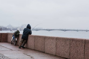 Saint-Petersburg, Rusya Federasyonu-Kasım 2015 yaklaşık: olta, Saint Petersburg'daki Neva Nehri'nin setin Sonbahar 2015 huysuz bir gün ile bir balıkçı.
