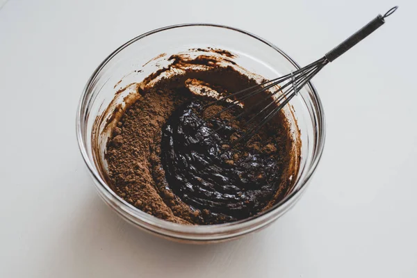 Un proceso de hacer salsa de chocolate: un tazón de vidrio con mezcla de chocolate en la superficie blanca . — Foto de Stock