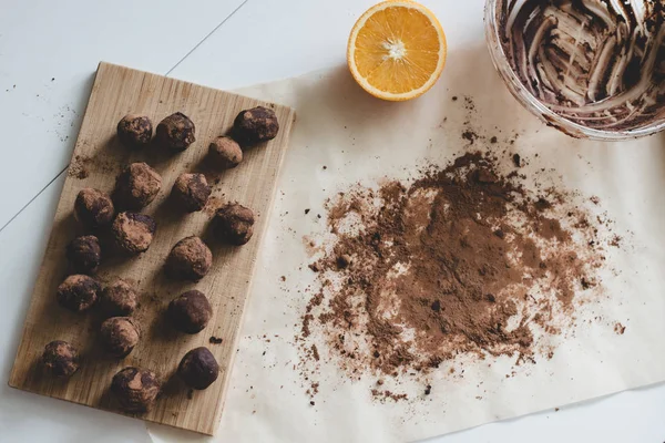 Gesundes Dessert: Schokoladentrüffel auf dem Holzbrett, eine Hälfte Orangen- und Kakaopulver auf dem Pergamentpapier. — Stockfoto