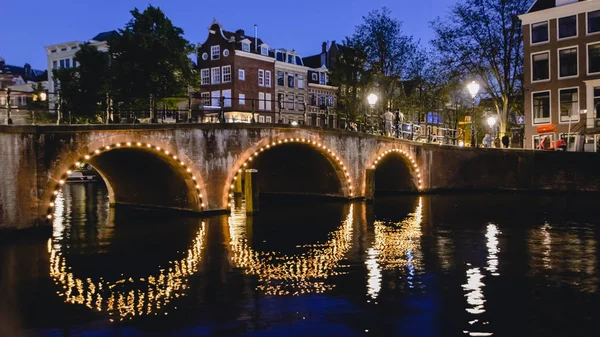 AMSTERDAM - CIRCA JUNIO 2017: vista de un puente con luces sobre un canal por la noche en junio de 2017 en Amsterdam, Países Bajos . — Foto de Stock