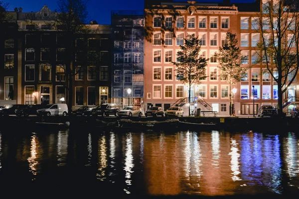 AMSTERDAM - CIRCA JUNIO 2017: vista nocturna de un canal con reflejos luminosos y edificios holandeses tradicionales en Amsterdam, Holanda en junio de 2017 . —  Fotos de Stock