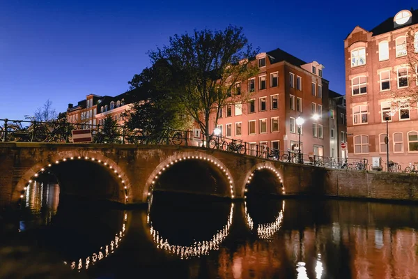 AMSTERDAM - CIRCA JUNIO 2017: vista de un puente con luces sobre un canal por la noche en junio de 2017 en Amsterdam, Países Bajos . — Foto de Stock