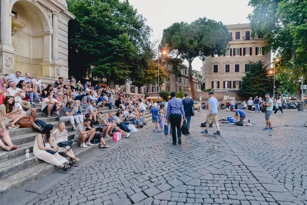 ROMA, ITALIA - CIRCA JUNIO 2017: la gente se sienta en un escalón de piedra en una animada plaza del barrio de Trastevere en Roma, Italia, en un soleado día de verano en junio de 2017 . — Foto de Stock