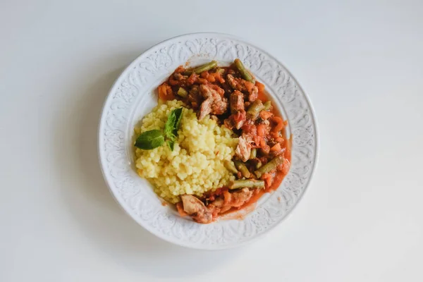 Cooked dish of moroccan cuisine: golden couscous with citrus and spicy chicken on a white plate on the white table. — Stock Photo, Image