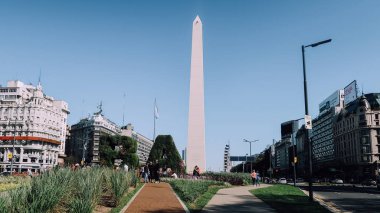 BUENOS AIRES, ARGENTINA - CIRCA ECTOBER 2019: Buenos Aires 'in sembolik simgesi Obelisk, güneşli bir sonbahar gününde güneşli bir gökyüzü ile birlikte çimenlerin ve bitkilerin ünlü BA işareti.