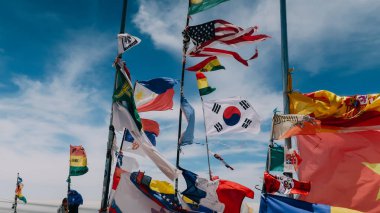 UYUNI, BOLIVIA - CIRCA NOVEMBER 2019: Güneşli bir günde, bulutlu mavi gökyüzü ile birlikte Uyuni Tuz Düz Çölü 'nde dünyanın birçok farklı bayraklarıyla bayrak istasyonu.
