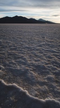 UYUNI, BOLIVIA - CIRCA Kasım 2019: Bulutlu gökyüzü ile gün batımında Salar de Uyuni 'nin sonsuz boş tuz çölü.