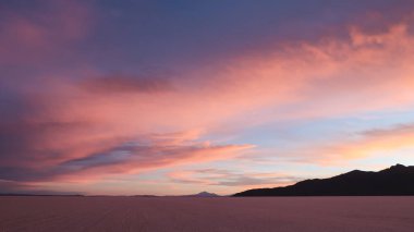 UYUNI, BOLIVIA - CIRCA NOVEMBER 2019: Salar de Uyuni 'nin sonsuz boş tuzlu çölü bulutlu gökyüzü ile parlak mor gün batımında.