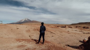 UYUNI, BOLIVIA - CIRCA NOVEMBER 2019: Siyah elbiseli kız bulutlu mavi gökyüzü ile güneşli bir günde Bolivya Altiplano 'da terk edilmiş bir dünyada duruyor.