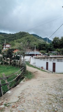 SANTANDER, COLOMBIA - CIRCA Aralık 2019: Dağların ve bulutlu gökyüzünün küçük eski köy manzarasında asfaltsız yol.