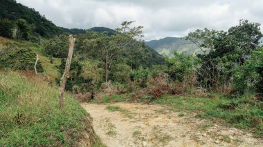 SANTANDER, COLOMBIA - CRCA Aralık 2019: Orman, yeşil tepeler ve bulutlu gökyüzü ile doğa yürüyüşü yolu.
