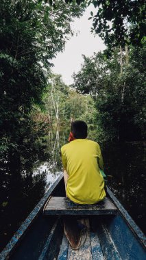 LETICIA, AMAZONAS, COLOMBIA - CRCA Aralık 2019: Güneşli bir günde Amazon ormanlarında yelken açan motorlu teknenin üstündeki sarı tişörtlü çocuk.