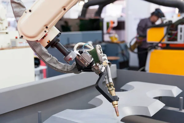 Ipari Hegesztő robot kar a fókuszban, homályos hegesztő a háttérben — Stock Fotó